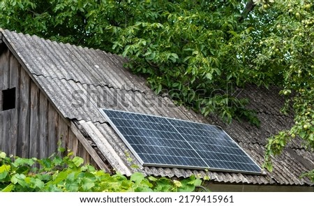 Solar panel on the roof of old barn in village in dense greenery of leaves Royalty-Free Stock Photo #2179415961