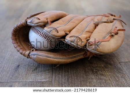 An old baseball inside an old well loved leather baseball glove, sitting on wooden floorboards Royalty-Free Stock Photo #2179428619