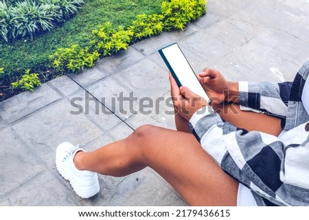 woman with cell phone in her hands sitting on the sidewalk in the garden of her house, cell phone on white.
