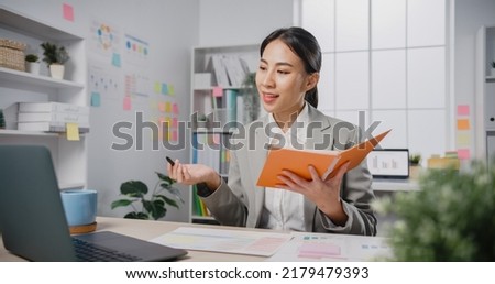 Young Asia cheerful professional woman sitting on desk with laptop computer hold agenda prepare present script public speak at office. Lady business suit, Speak skill for job career self improve. Royalty-Free Stock Photo #2179479393