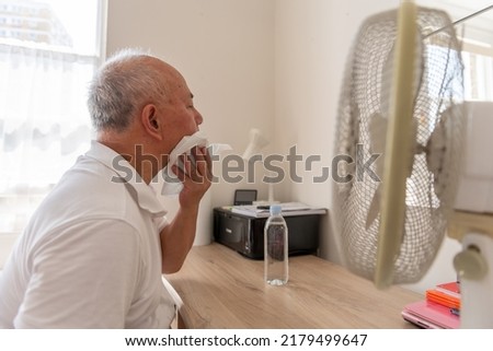 A senior man suffering from extreme hot, record breaking summer heat, trying to keep cool and well at home. Royalty-Free Stock Photo #2179499647