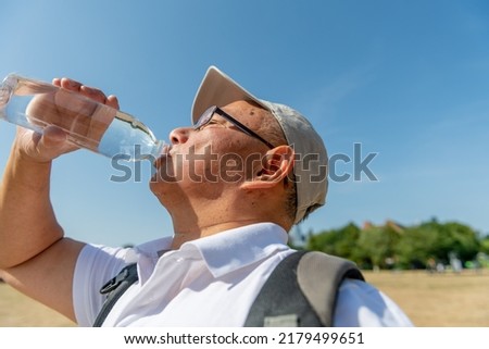 A senior man drinking plenty of water on a record breaking hot summer day to avoid dehydration while out and about. Royalty-Free Stock Photo #2179499651