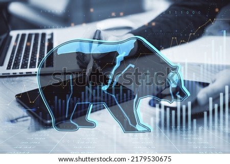  hands at desktop using smartphone and digital tablet with pen and abstract hologram of bear on financial stock market graph representing stock market crash or down trend investment 