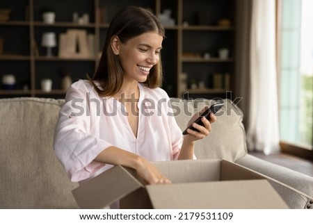 Happy woman unbox parcel box, check ordered items in phone use retail ecommerce application, leave positive feedback to customer, feel satisfied with delivered goods, quick delivery services concept Royalty-Free Stock Photo #2179531109
