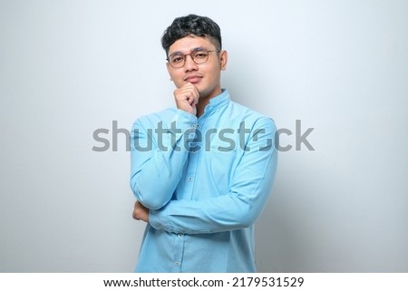 Handsome young asian man wearing casual clothes over white background looking confident at the camera smiling with crossed arms and hand raised on chin. thinking positive.