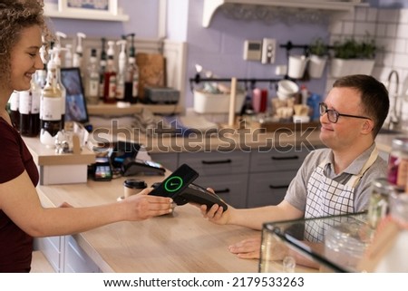 Caucasian waiter with down syndrome accepting contactless payment in the cafe