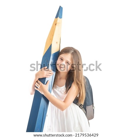 Cute little girl with a school bag holds a huge blue pencil in her hands - Isolated on white.