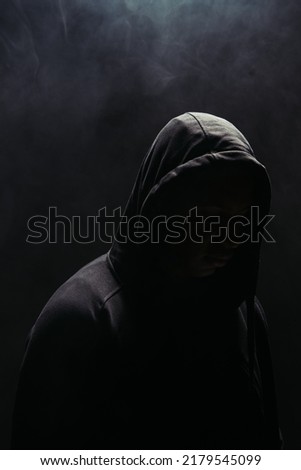 Silhouette of bandit in hoodie on black background with smoke