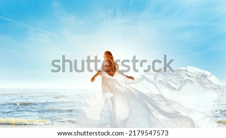 Model in White Dress Flying on Wind. Happy Woman Enjoying Sun looking away at Blue Sky. Carefree Girl dreaming at Sea Beach Resort. Freedom and Spiritual Relax Concept Royalty-Free Stock Photo #2179547573