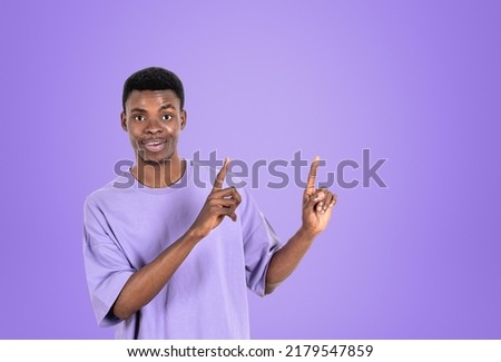 African American businessman wearing casual wear is standing pointing up with fingers near empty purple wall in background. Concept of model, successful business person, show