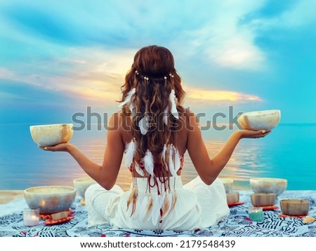 Woman with Tibetan Singing Bowls. Relaxation and Meditation at Sunset Beach. Sound Healing Therapy. Peaceful Women Silhouette practicing Yoga over Sunrise Sky Royalty-Free Stock Photo #2179548439