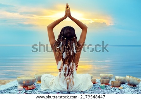 Yoga Meditation at Sunset Beach. Peaceful Woman relaxing with Tibetan Singing Bowls. Indian Women Silhouette meditating over Sunshine Blue Sky background Royalty-Free Stock Photo #2179548447