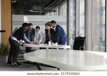 Serious diverse business project group meeting at table in modern office, talking over paper reports, sharing ideas, decision, problem solving. Indian corporate coach teaching team of new employees Royalty-Free Stock Photo #2179550065