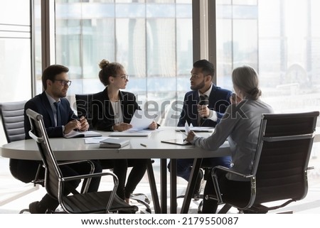 Busy millennial professional group reviewing startup marketing reports, collaborating on project. Business partners negotiating on deal, discussing agreement terms on meeting in office Royalty-Free Stock Photo #2179550087