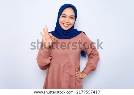 Cheerful young Asian muslim woman in pink shirt showing okay gesture demonstrates symbol of approval isolated over white background. People religious lifestyle concept