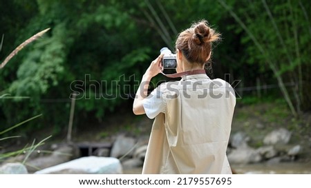Hipster young Asian female taking a picture of the beautiful forest with her retro film camera. Outdoor and camping concept.