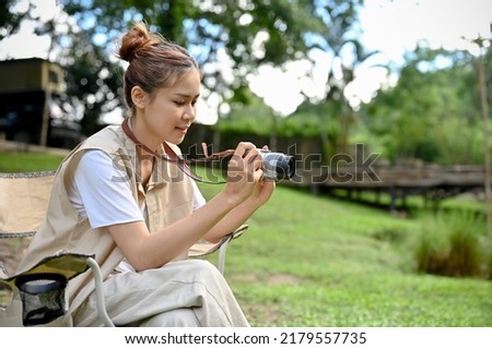 Attractive and hipster young Asian female taking a picture of the beautiful forest with her retro film camera. Outdoor and camping concept.