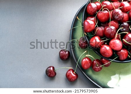 beautiful ripe cherries spilled out of the plate on a gray background