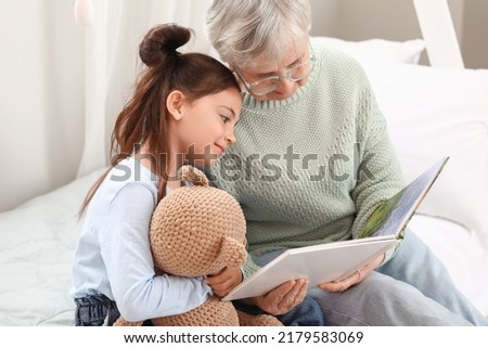 Little girl with toy and her grandma reading book in bedroom