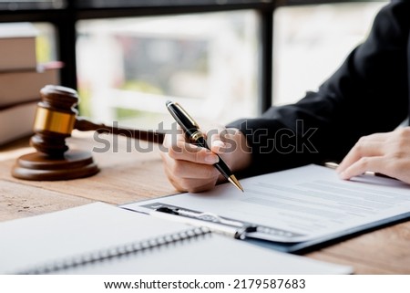 A lawyer sits in his office, on a table with a small hammer to beat the judges desk in court. and justice scales, lawyers are drafting a contract for the client to use with the defendant to sign. Royalty-Free Stock Photo #2179587683