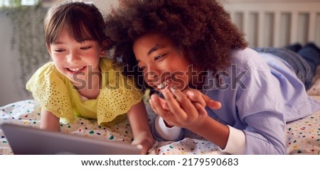 Girl And Boy In Bedroom Lying On Bed Using Digital Tablet Together