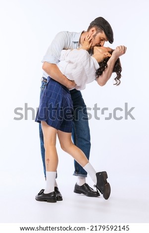 Portrait of young beautiful couple, man and woman, in retro putfit kissing isolated over white studio background. Concept of vintage fashion, hobby, activity, art, music, party, creativity and ad