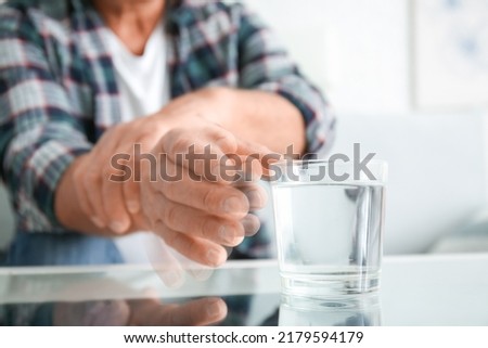 Senior man with Parkinson syndrome taking glass of water from table, closeup Royalty-Free Stock Photo #2179594179