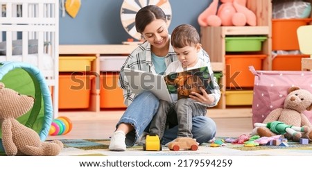 Nanny and little boy reading interesting book in room Royalty-Free Stock Photo #2179594259