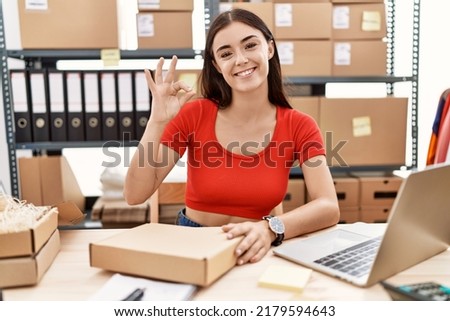 Young hispanic woman preparing order working at storehouse smiling positive doing ok sign with hand and fingers. successful expression. 