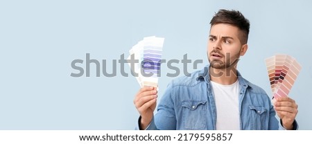 Confused young man with color palettes on light blue background with space for text