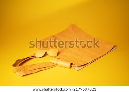 Bag with sunscream and sunglasses on a yellow background. - Summer concept	
