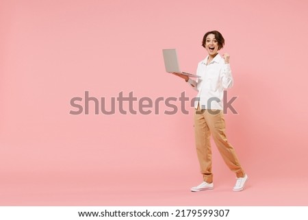 Full length young employee business woman corporate lawyer in classic white shirt work in office hold laptop pc computer chat online do winner gesture clench fist isolated on pastel pink background.