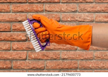 Close-up view of woman's hand in rubber protective glove with a plastic brush and a brick wall on the background. Cleaning concept.