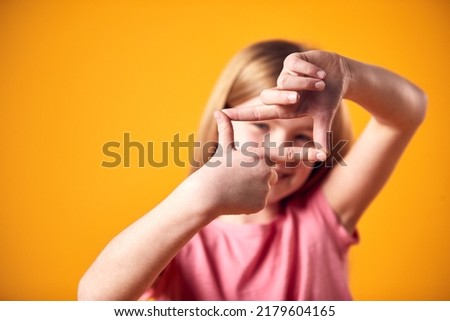 Studio Portrait Of Smiling Girl Making Shape Of Picture Frame With Hands Against Yellow Background