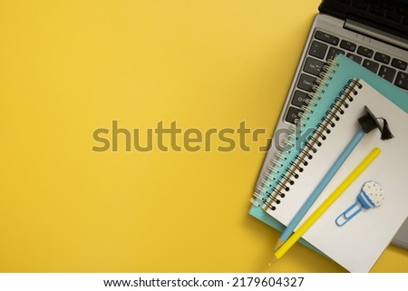 Colorful pencils with graduated cap and note on laptop on colored background. Copy space. Children work space top view, flat lay.