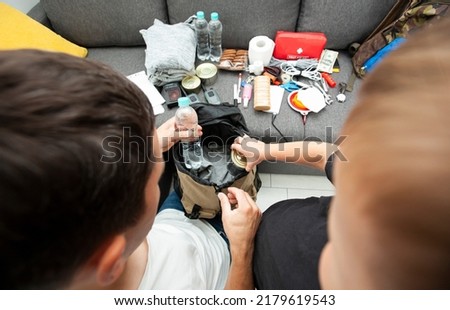 Father and son assemble the emergency evacuation bag together and put necessary items into backpacks Royalty-Free Stock Photo #2179619543