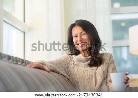 Older woman sitting on the sofa drinking coffee. Royalty-Free Stock Photo #2179630341