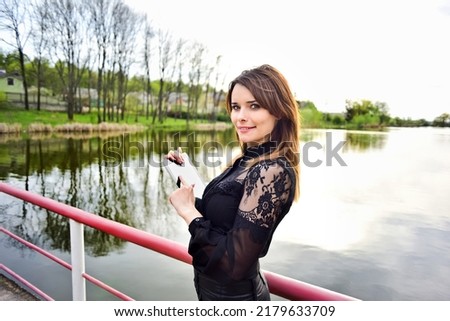 smiling woman holding tablet near lake