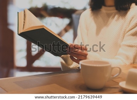 Woman with coffee reading book at wooden table, closeup