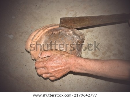 Rough hands are peeling the dried coconut with an old knife.