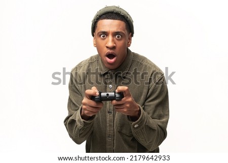 Excited young multiracial man playing video games and looking at camera with surprised face, holding wireless joystick console isolated over white background. Gamer concept