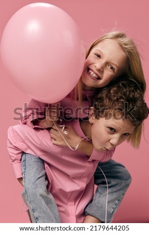joyful, happy children of school age, on a pink background in pink clothes play and the boy rolls the girl with a balloon on her back