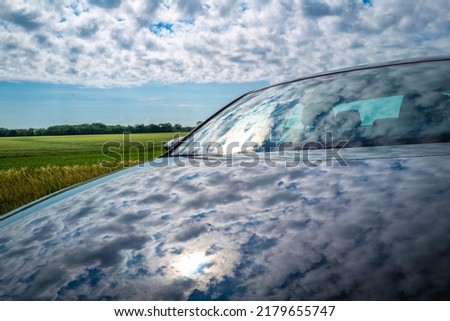 Abstract colors and texture of the clouds reflected on the car hood and windshield with cornfield prairie of North Dakota in the background.