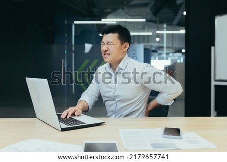 Asian businessman working in office, having severe back pain, overtired worker working with laptop. Royalty-Free Stock Photo #2179657741