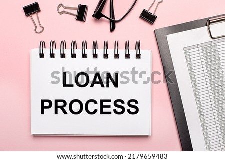 On a pink background, reports, black paper clips, glasses and a white notebook with the text LOAN PROCESS