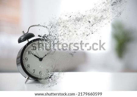 Time is running out. Black alarm clock vanishing on table in room Royalty-Free Stock Photo #2179660599