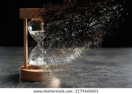 Time is running out. Hourglass vanishing on grey table against black background