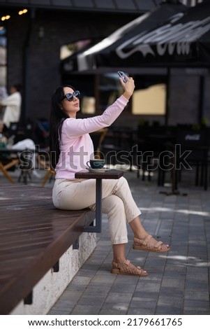 Beautiful American girl taking selfie with mobile phone while having breakfast at coffee shop