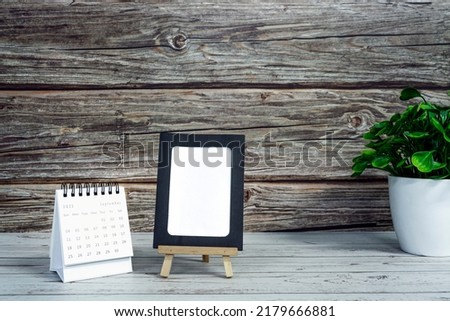 White September 2022 calendar on wooden desk with paper frame and potted plant. 2022 new year concept. Copy space.