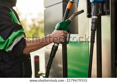 Side view of crop unrecognizable male in uniform inserting fuel nozzle into dispenser after filling vehicle during work at gas station Royalty-Free Stock Photo #2179679555